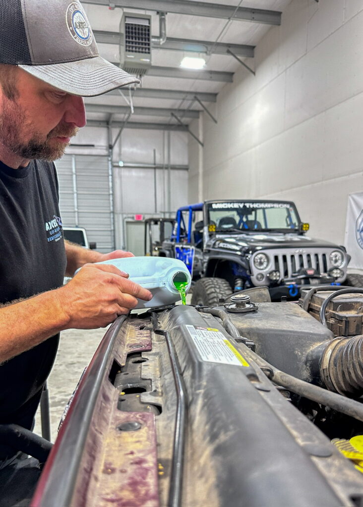 Chris Warden, owner of Axcell Off Road and Performance, adds engine coolant to a vehicle in his shop.